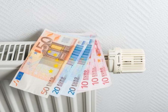 Des billets de banque en euros posés sur un radiateur blanc à côté de sa valve thermostatique.