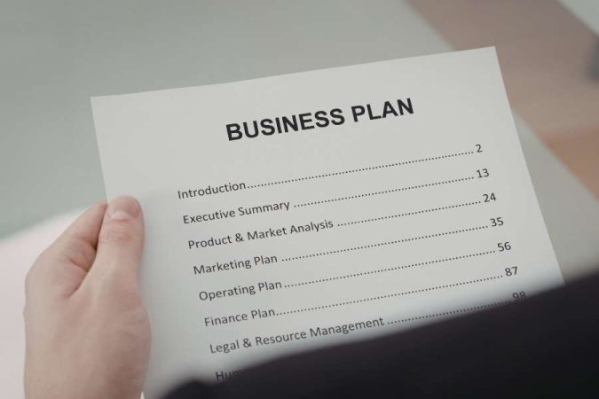 Gros plan sur la table des matières d'un document imprimé intitulé "BUSINESS PLAN" tenu par une main.