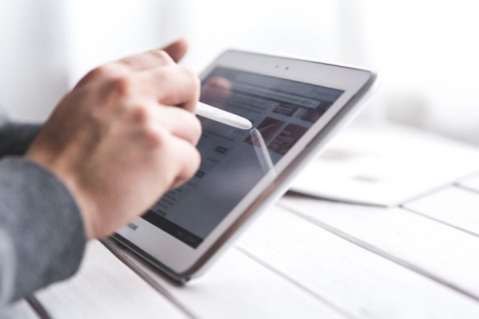 Une main utilise un stylet sur une tablette tactile pour naviguer sur un site web ou des applications mobiles.