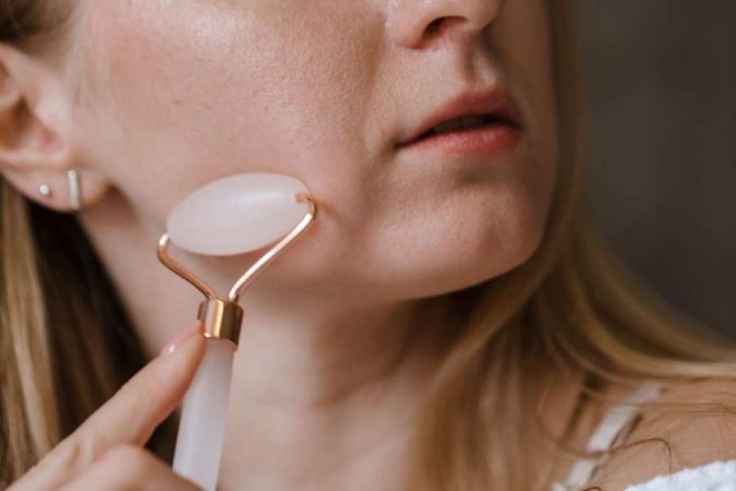 Une femme utilise un rouleau de jade pour purifier sa peau et détendre son visage.