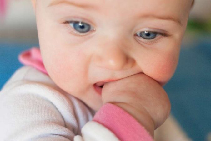Un bébé aux yeux bleus qui mordille son poing parce qu'il fait ses dents.