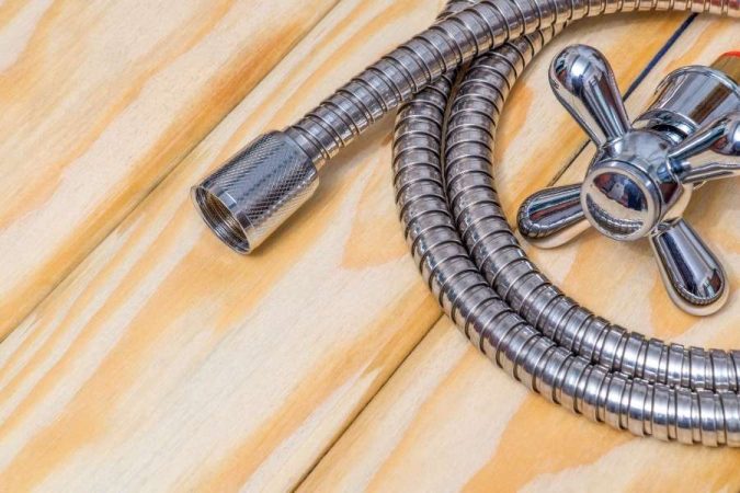 Un flexible de douche en métal chromé et une poignée de robinet posés sur un plan en bois clair.